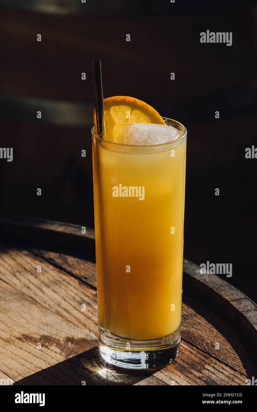 orange juice drink in tall glass with gold straw, sitting on whiskey