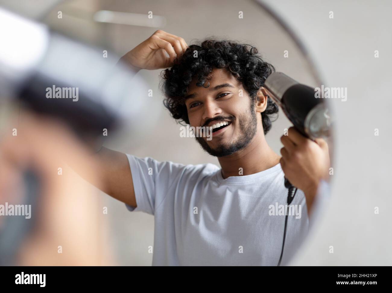 Excited indian man using hairdryer after shower, drying his curly hair