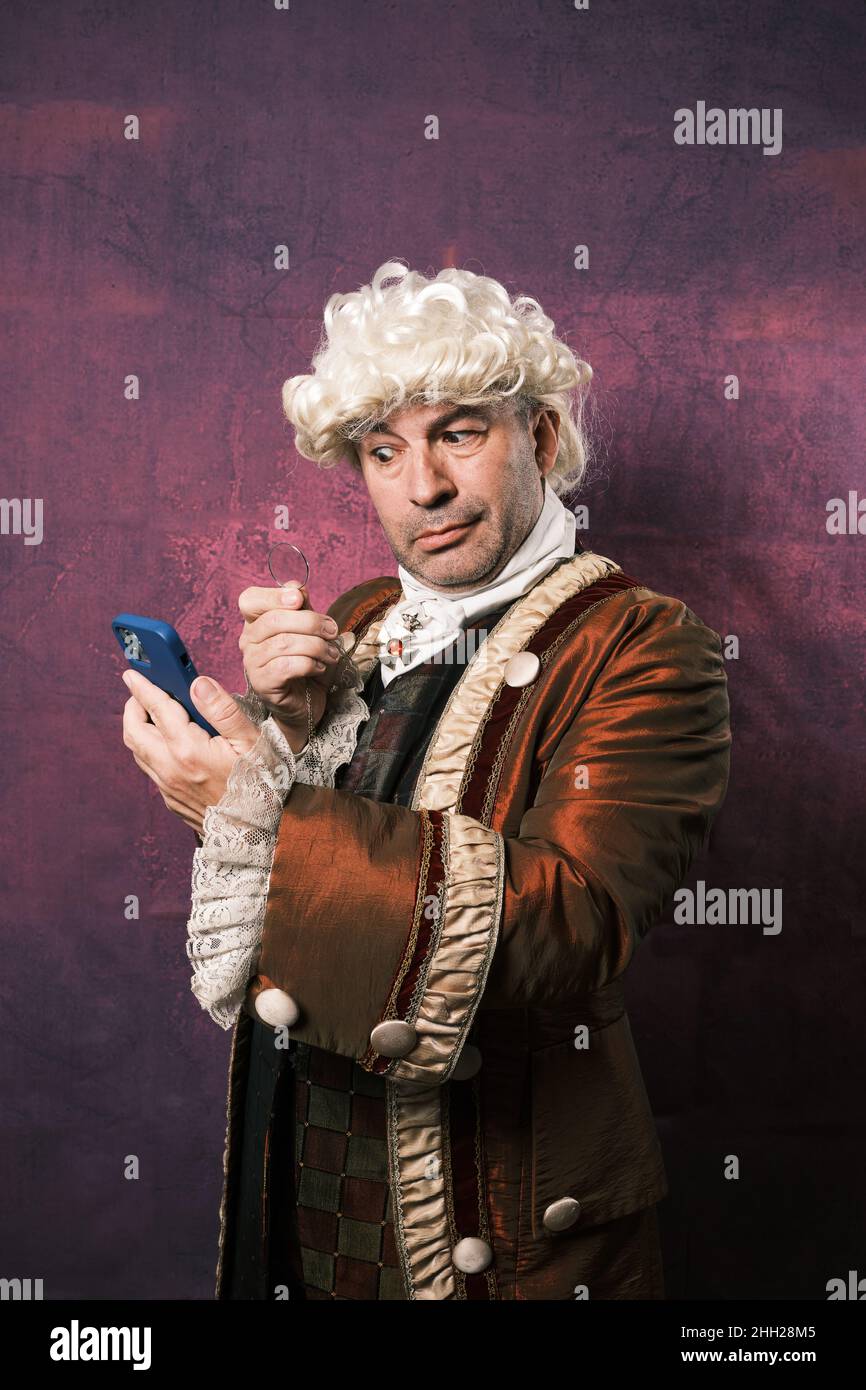 Man in classic renaissance clothes using an old monocle to see the mobile phone screen. Stock Photo