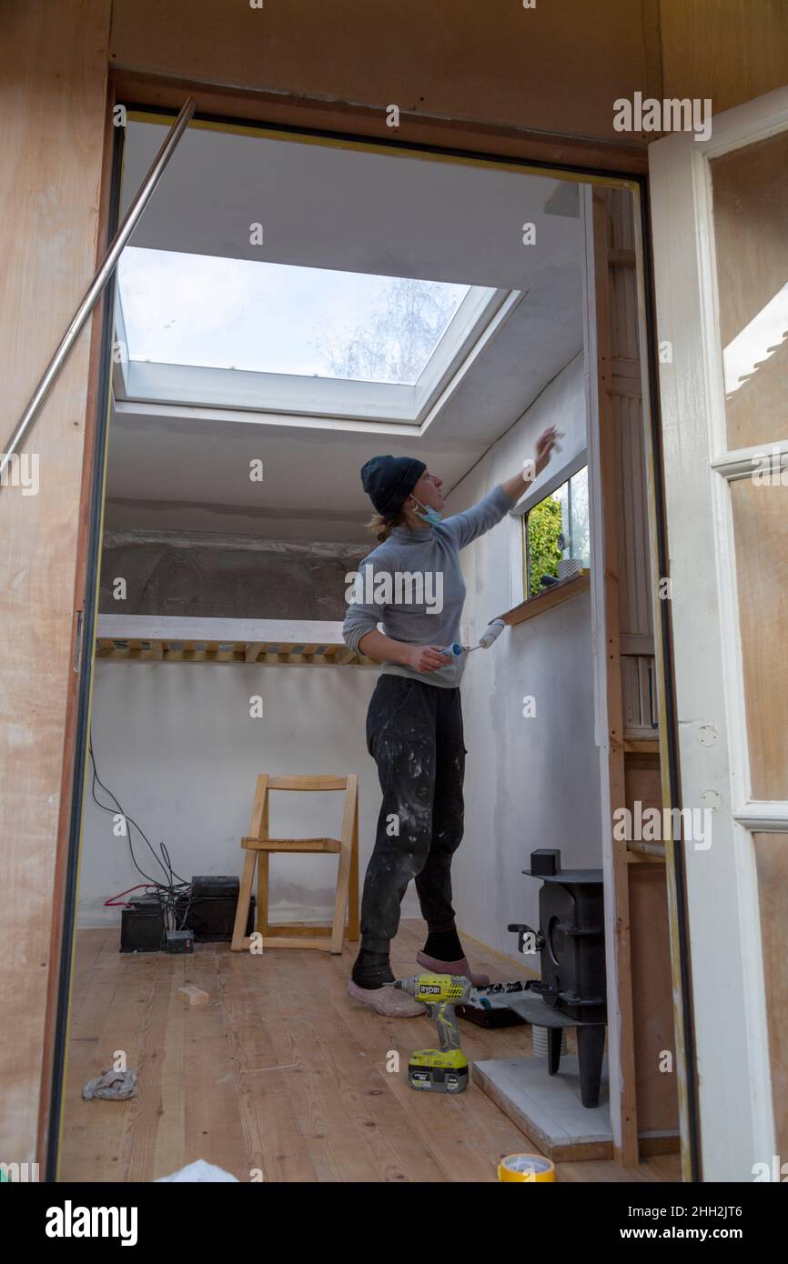 Young woman painting Luton van interior as part of a conversion project, UK Stock Photo