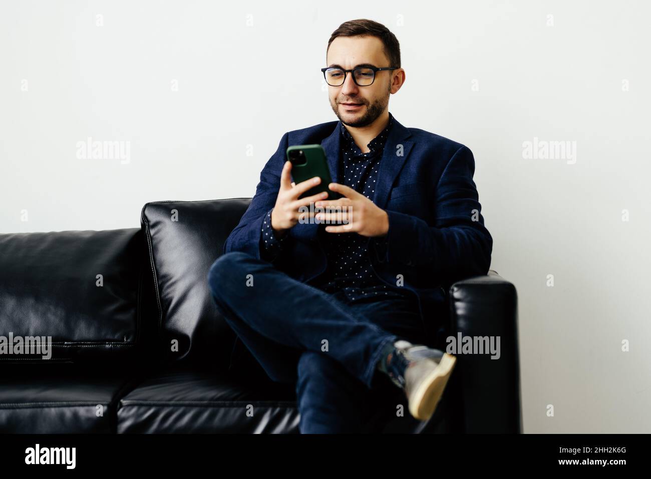 Focused young guy spend time on couch use ecommerce software on mobile telephone check email in convenient client app. Stock Photo