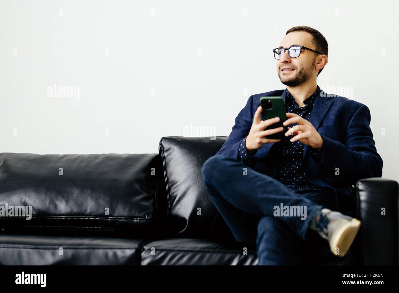 Focused young guy spend time on couch use ecommerce software on mobile telephone check email in convenient client app. Stock Photo