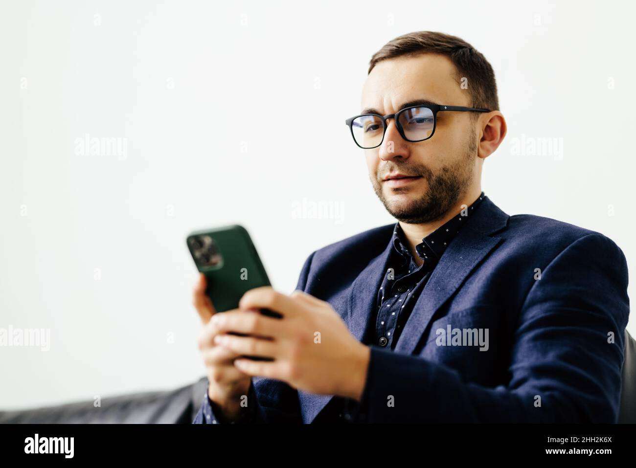 Focused young guy spend time on couch use ecommerce software on mobile telephone check email in convenient client app. Stock Photo