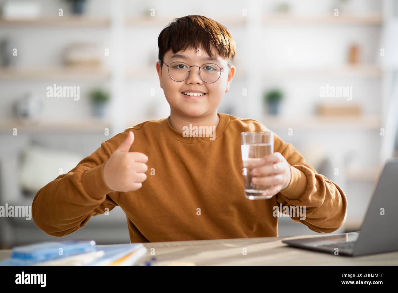 Healthy japanese teenager holding glass of water while studying Stock