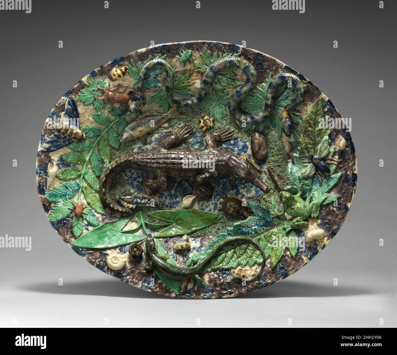 Platter with crocodile, snake, and lizard ca. 1870–80 School of Paris Inspired by the works made by the Renaissance ceramicist Bernard Palissy (1510-ca.1590), nineteenth-century producers of Palissy ware combined novel motifs with traditional techniques. A crocodile, which were not a typical feature of the sixteenth-century potter’s work, occupies the center of this platter teeming with life.. Platter with crocodile, snake, and lizard. French. ca. 1870–80. Glazed earthenware. Ceramics-Pottery Stock Photo