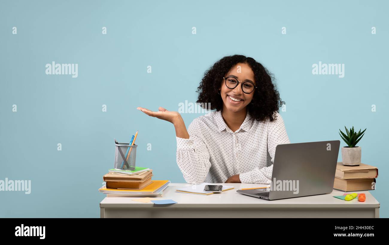 Cheerful young black female student sitting at table with laptop ...