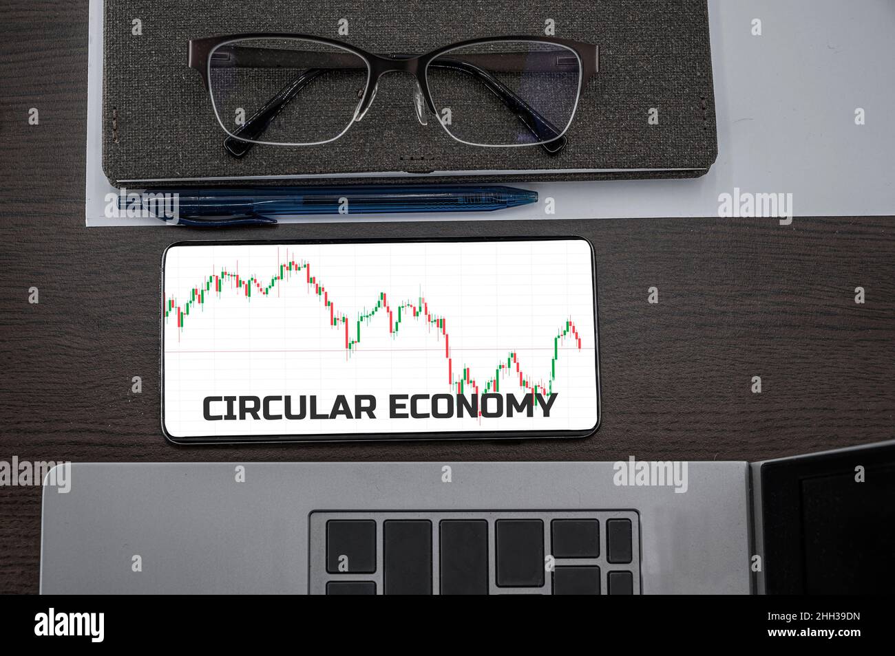 Circular economy concept. Top view of stocks price candlestick chart in phone on table near laptop, notepad and glasses with inscription circular econ Stock Photo