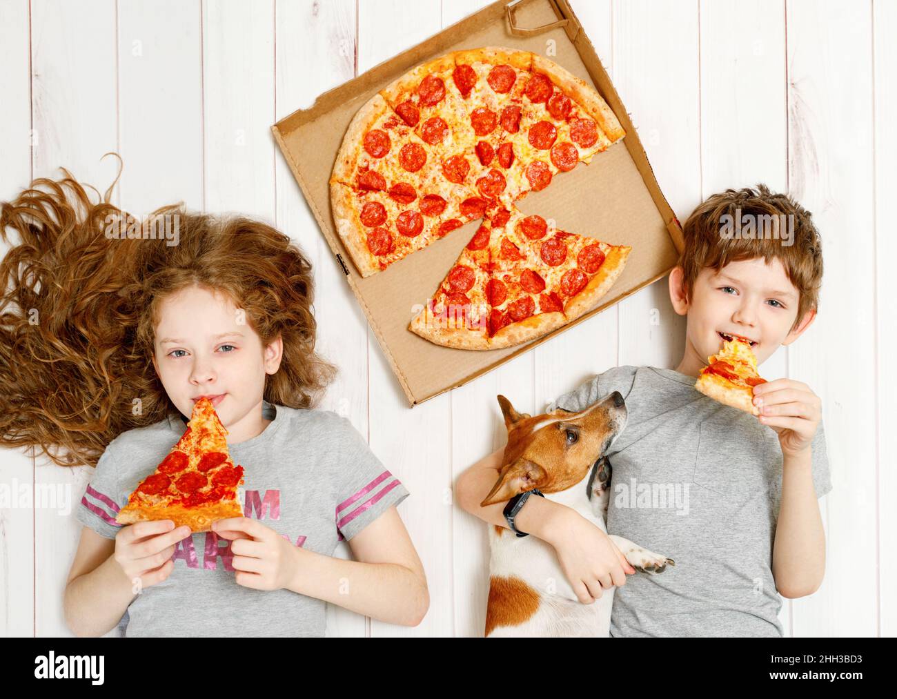 Kids and dog eating pepperoni pizza. Children holding a slices of pizza