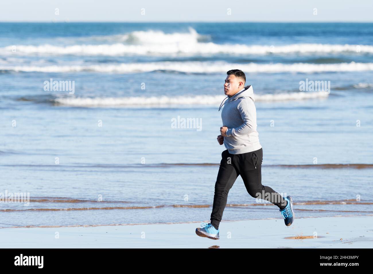 Hispanic man running at seaside, focused on his goals Stock Photo