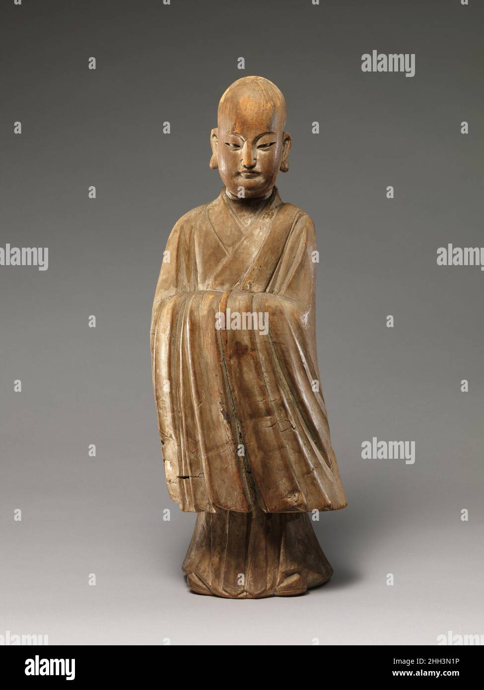 Arhat (Luohan) 16th–17th century China This sculpture epitomizes the merging of religious and secular imagery in later Chinese Buddhist sculpture. With his shaven head and elongated earlobes, the figure resembles a luohan (one of the Indian disciples of the Buddha), but his refined facial features, dignified posture, long-sleeved robe, and pointed shoes—all attributes associated with Confucian scholar-officials—identify him unmistakably as a youthful monk.The sculpture’s tendency toward abstraction and stylization—the contours of the head, body, and robes are conveyed through the buildup of si Stock Photo