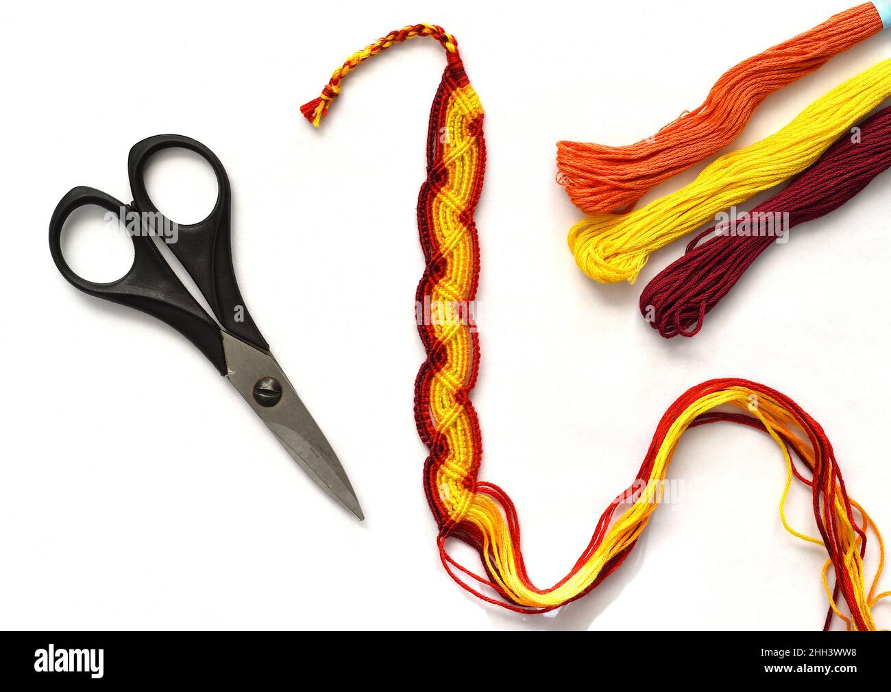 Unfinished woven DIY friendship bracelet with boho pattern next to scissors on white background Stock Photo