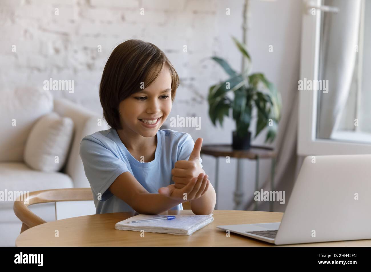 Smiling boy with hearing disability studying online from home Stock Photo