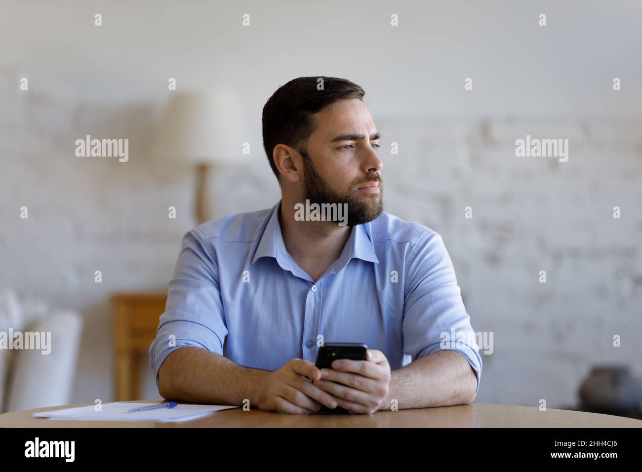Thoughtful pensive millennial smartphone user man looking away Stock Photo