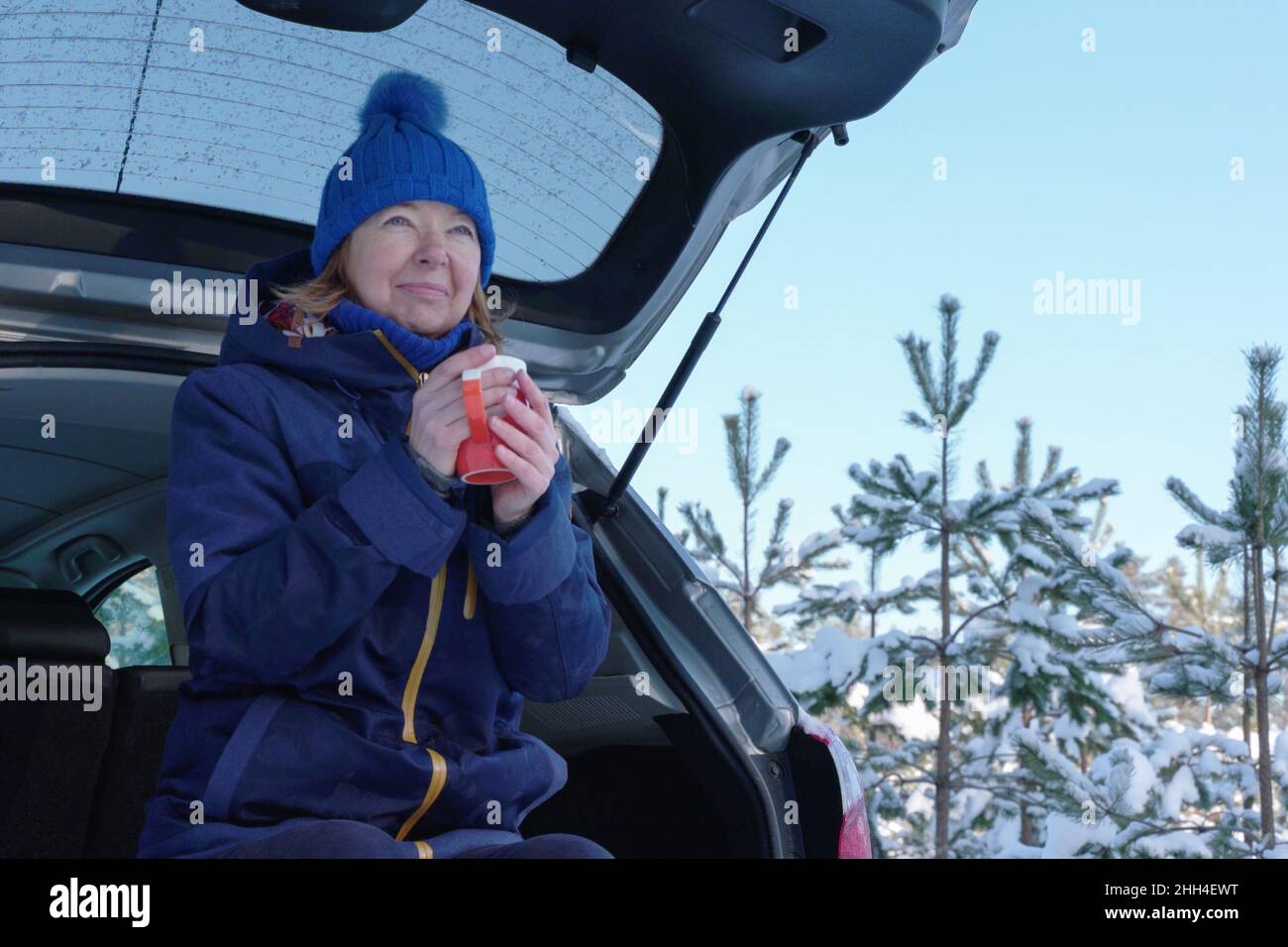 Mature skier having tea while sitting in back of suv after wintry forest trail. Outdoor activities to boost mood during coronavirus pandemic at winter Stock Photo