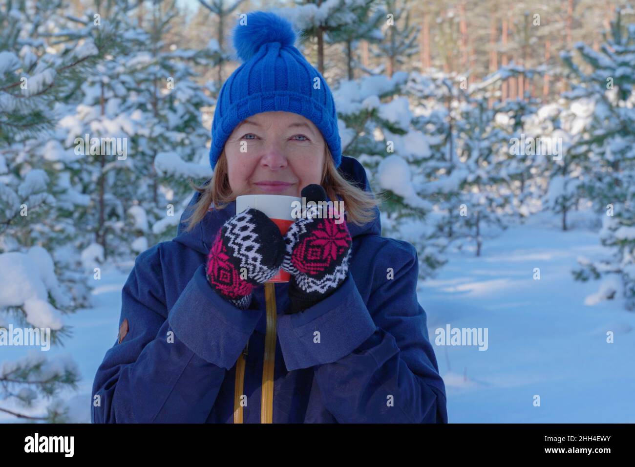 Portrait of smiling fit retired senior woman having tea after outdoor activity winter forest at snowy winter day. Active lifestyle in senior age Stock Photo