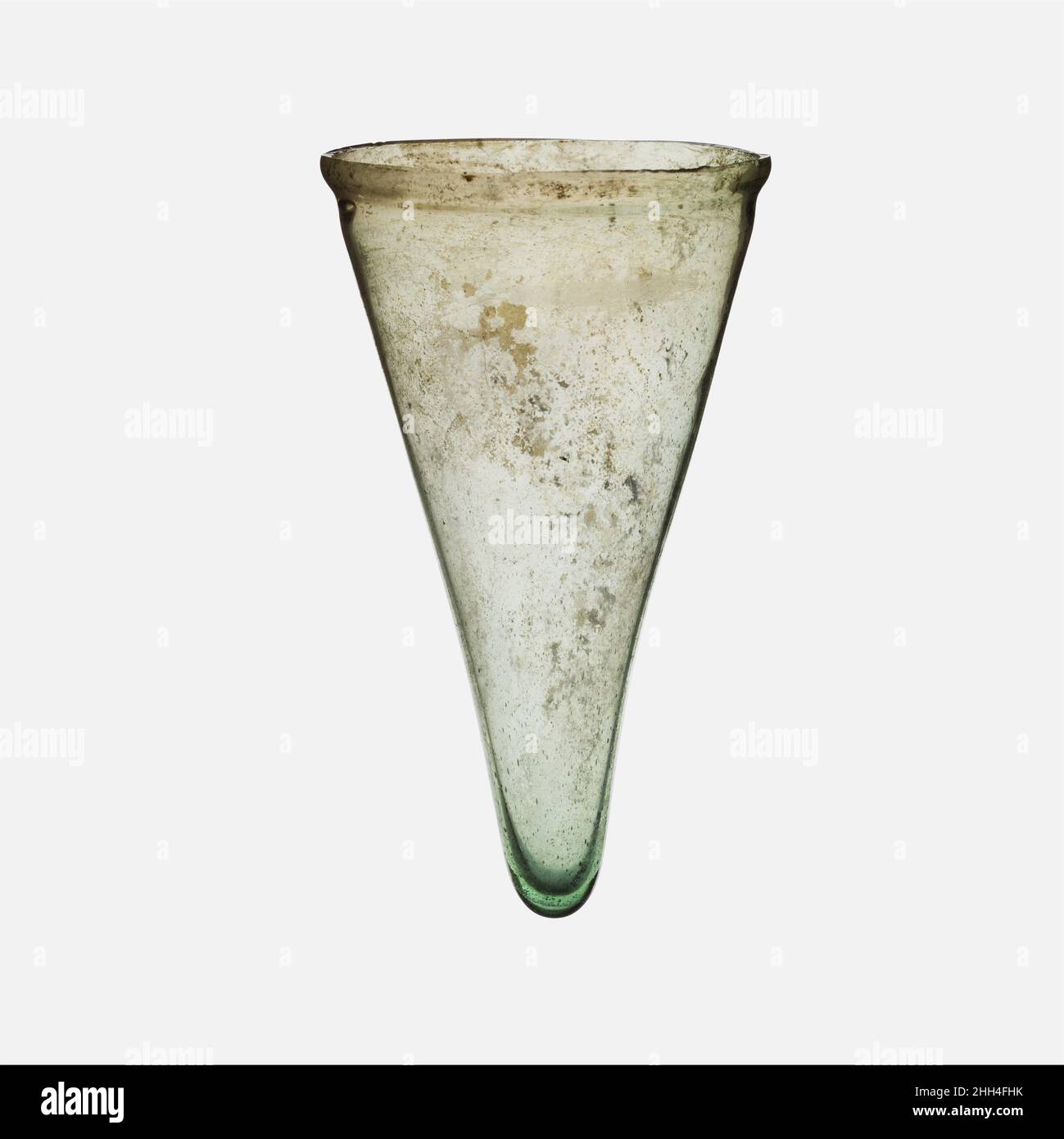 Glass lamp 4th century A.D. Roman Translucent pale green with bluish tingeUnworked, uneven, knocked off rim; narrow bulging collar below; almost straight sides tapering to pointed, thick bottom, with small flattened pad at tip.Intact; pinprick and some larger bubbles; some pitting, dulling, and iridescence on one side on exterior.. Glass lamp. Roman. 4th century A.D.. Glass; blown. Late Imperial. Glass Stock Photo