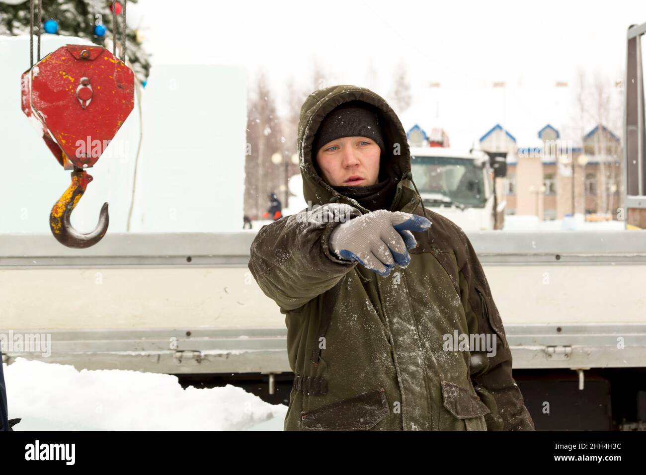 Portrait of a worker in a green jacket with a hood at the hook of a truck crane loading ice blocks Stock Photo