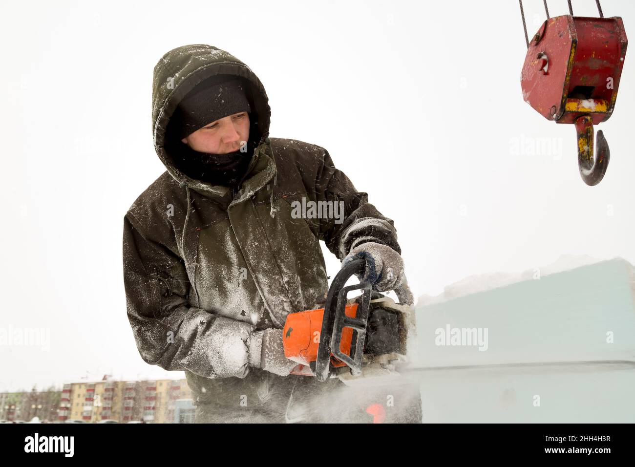 Portrait of a worker in a green jacket with a hood at the hook of a truck crane loading ice blocks Stock Photo