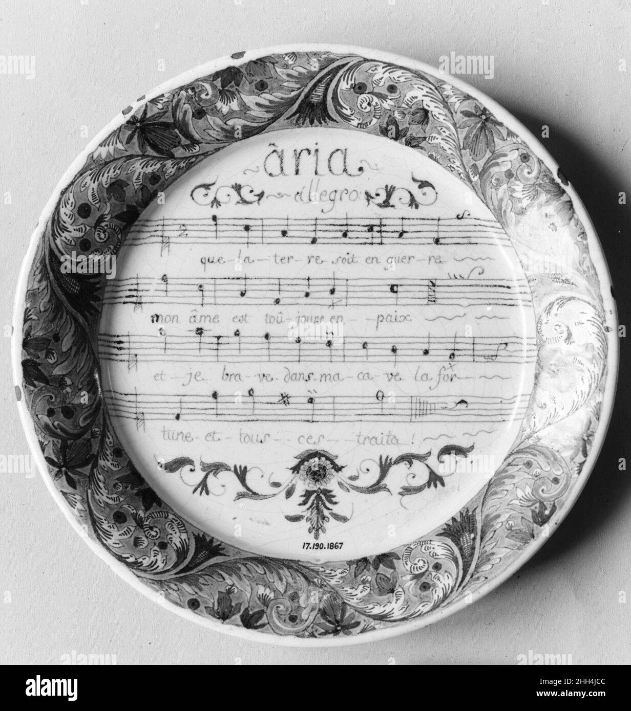 Plate ca. 1740 French, Rouen This plate is made of Rouen ware, a distinctive type of faience, or tin-enameled earthenware, produced in the Norman city of Rouen from the fifteenth century through the eighteenth. The elaborate border of floral scrolls on this example surrounds four staves of music simply titled 'Aria.' Although the opera for which the piece was composed has not been identified, its lyric is suited to the pastoral comic genre that was popular in France in the early eighteenth century. It translates as follows: 'Though the world be at war, my soul is still at peace, and in my cave Stock Photo