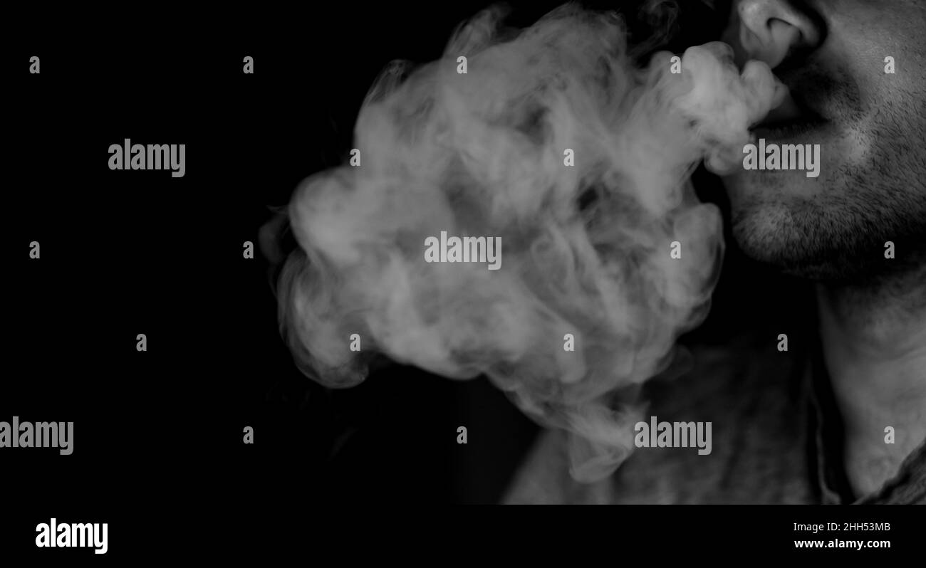 man will blow out clouds of white smoke on a black background. don't smoke Stock Photo