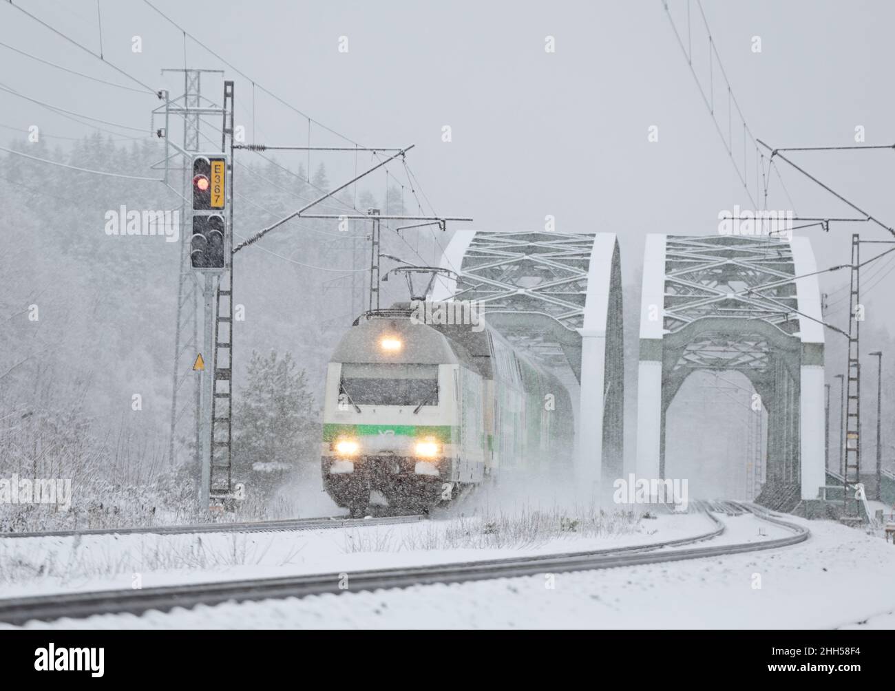 Passenger train in heavy snowfall coming out of railroad bridge Stock Photo