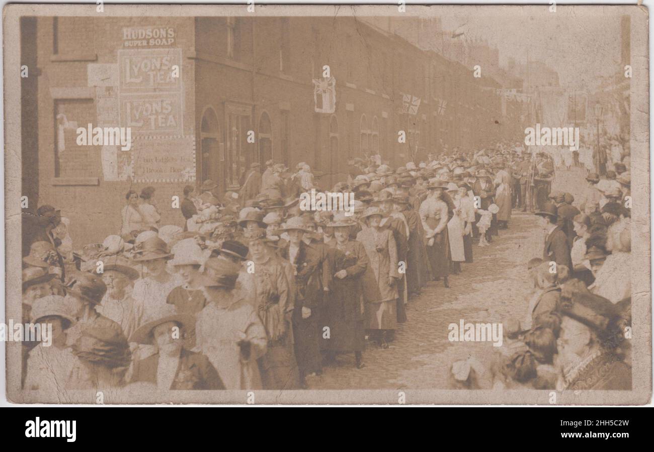 Parade through a Preston street, early 20th century. A group of women (all wearing hats) are at the front of the parading group, a military band is behind them. Flags, including the Union Jack, are hanging from the houses. Advertisements for Hudson's 'Super Soap', Lyons Tea and Brooke Bond Edglets Tea are on the side of one house Stock Photo