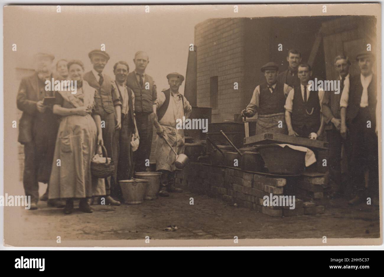 Soup kitchen, early 20th century: working men and women standing next to an outside cooking range with big pans on. One man has a large ladle, a woman is carrying a basket, and two buckets are on the floor Stock Photo
