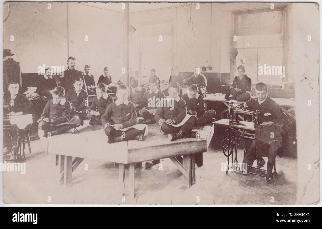 Borstal Boys, early 20th century: Boys being trained as tailors, watched by a guard. Several boys are using a treadle sewing machine and the others are hand sewing. The first Borstal (shown here) was founded in 1902 in the village of Borstal, near Rochester, Kent Stock Photo