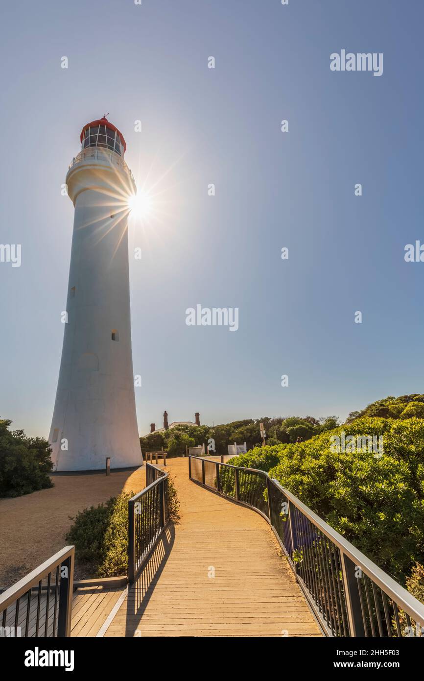 Split Point Lighthouse standing against shining sun with boardwalk in foreground Stock Photo