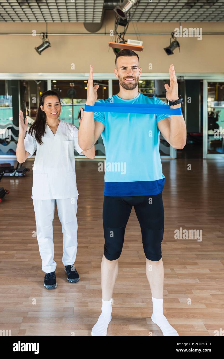 Fitness instructor guiding sportsman to exercise with equipment in gym