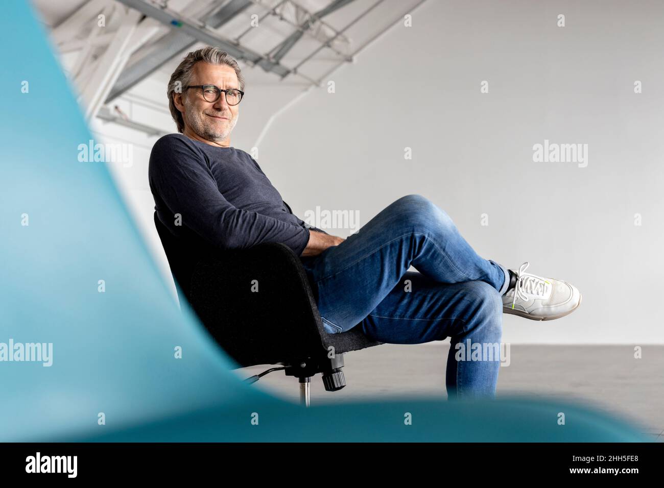 Smiling businessman sitting with legs crossed at knee on chair Stock Photo