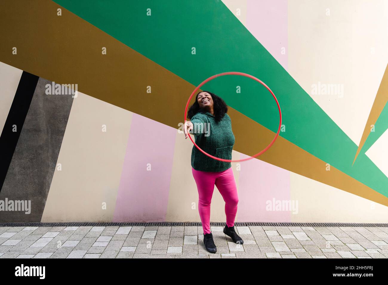Cheerful plus size woman playing with plastic hoop on footpath Stock Photo