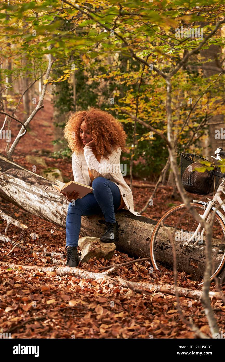 Woman reading book sitting on log in autumn forest Stock Photo