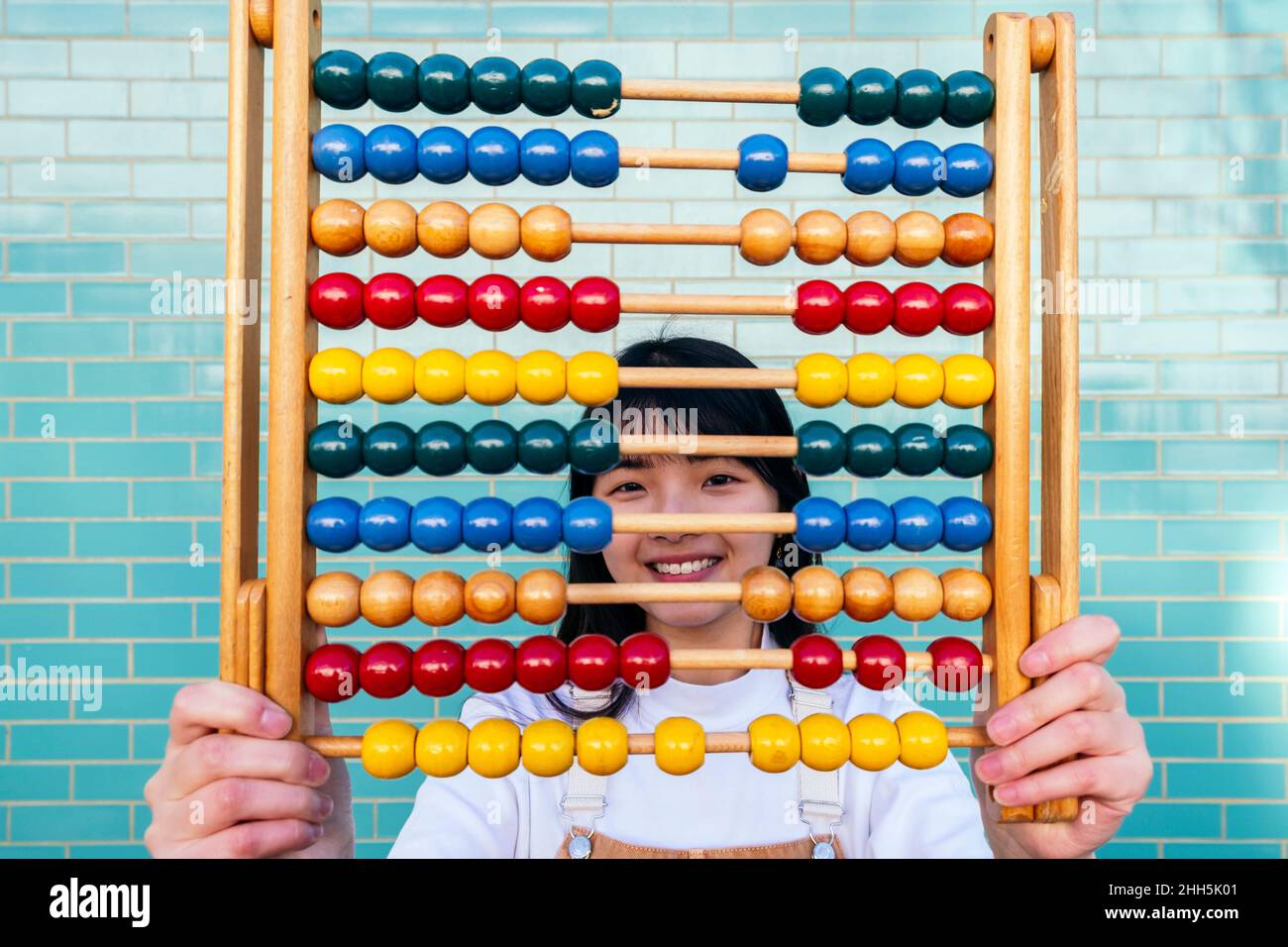 Smiling young woman holding abacus in front of brick wall Stock Photo