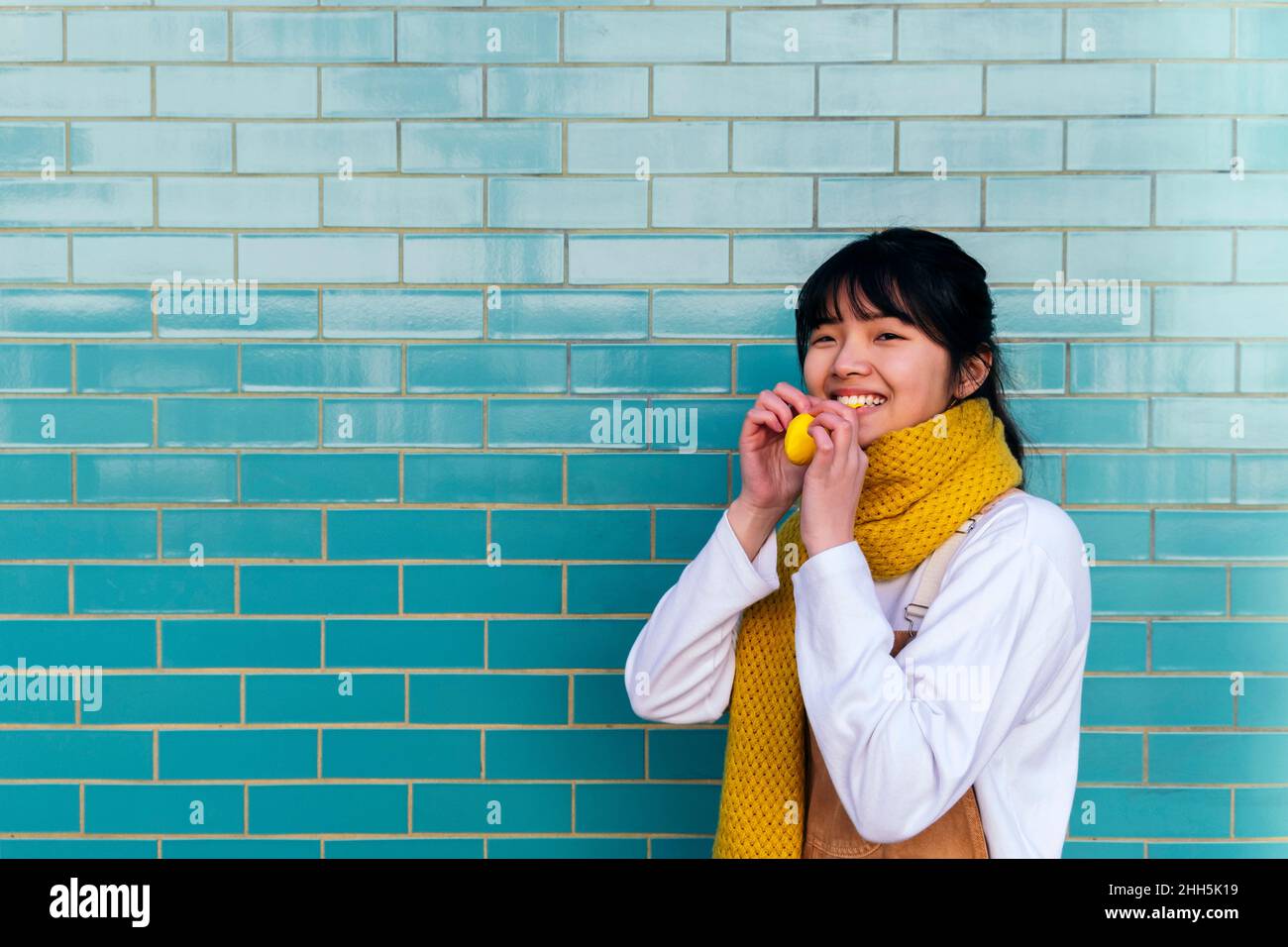 Smiling woman holding balloon in front of brick wall Stock Photo
