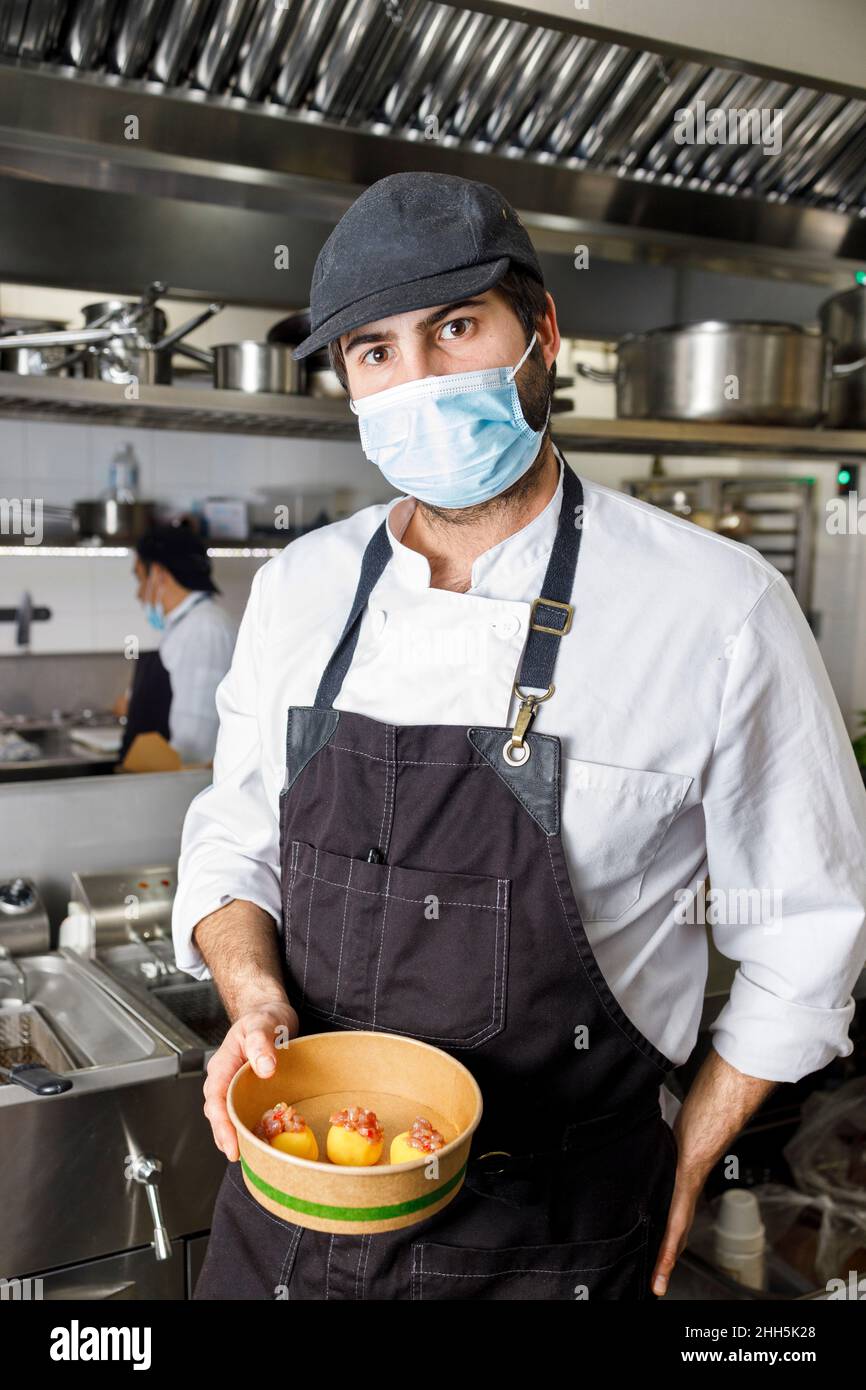 Chef with protective face mask holding dessert bowl at restaurant kitchen Stock Photo