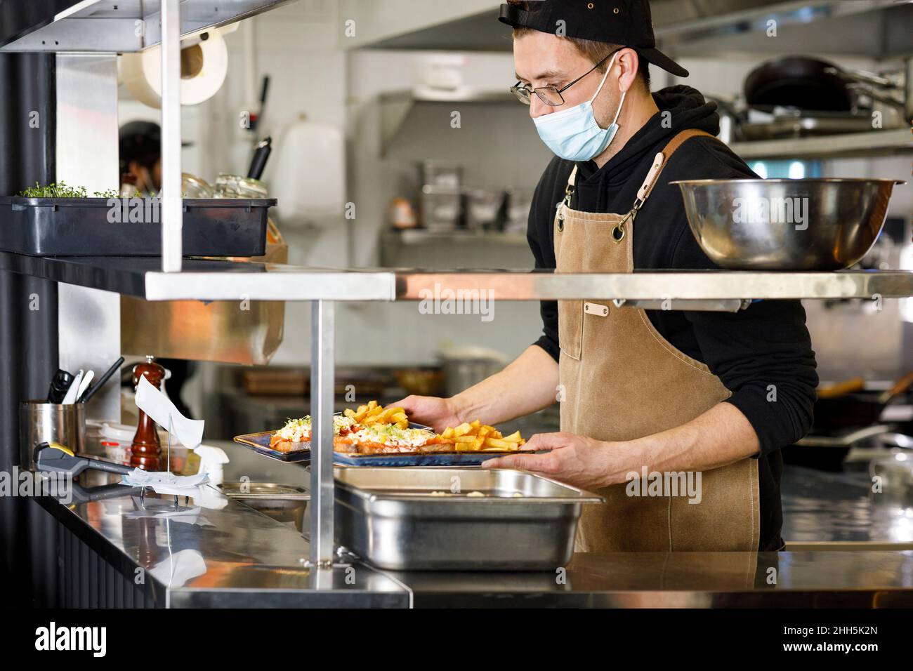 Chef with protective face mask holding food plates at restaurant kitchen Stock Photo