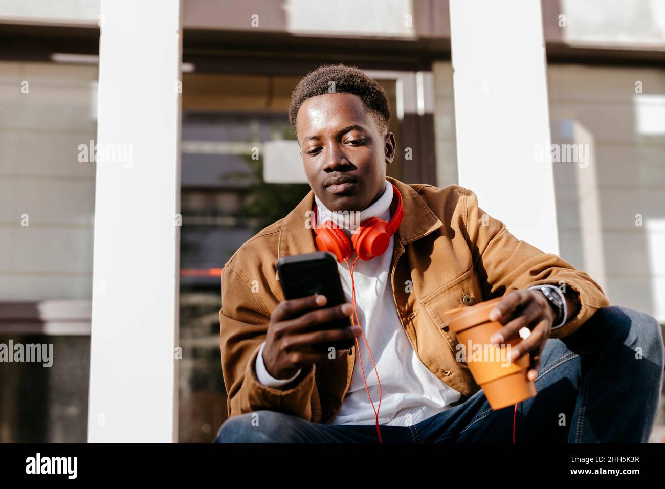 Young man holding reusable cup using smart phone Stock Photo