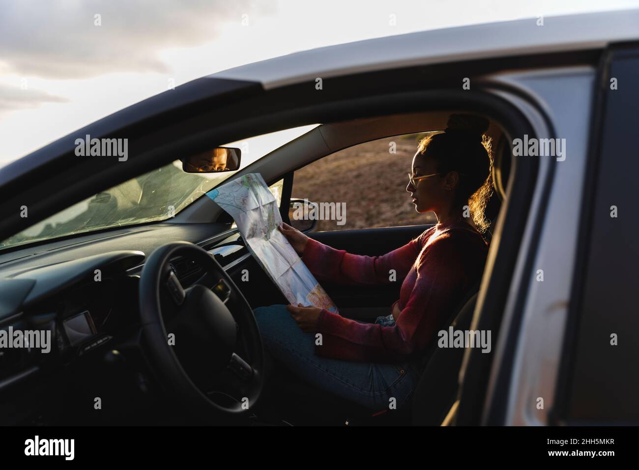 Young woman checking map in car at sunset Stock Photo