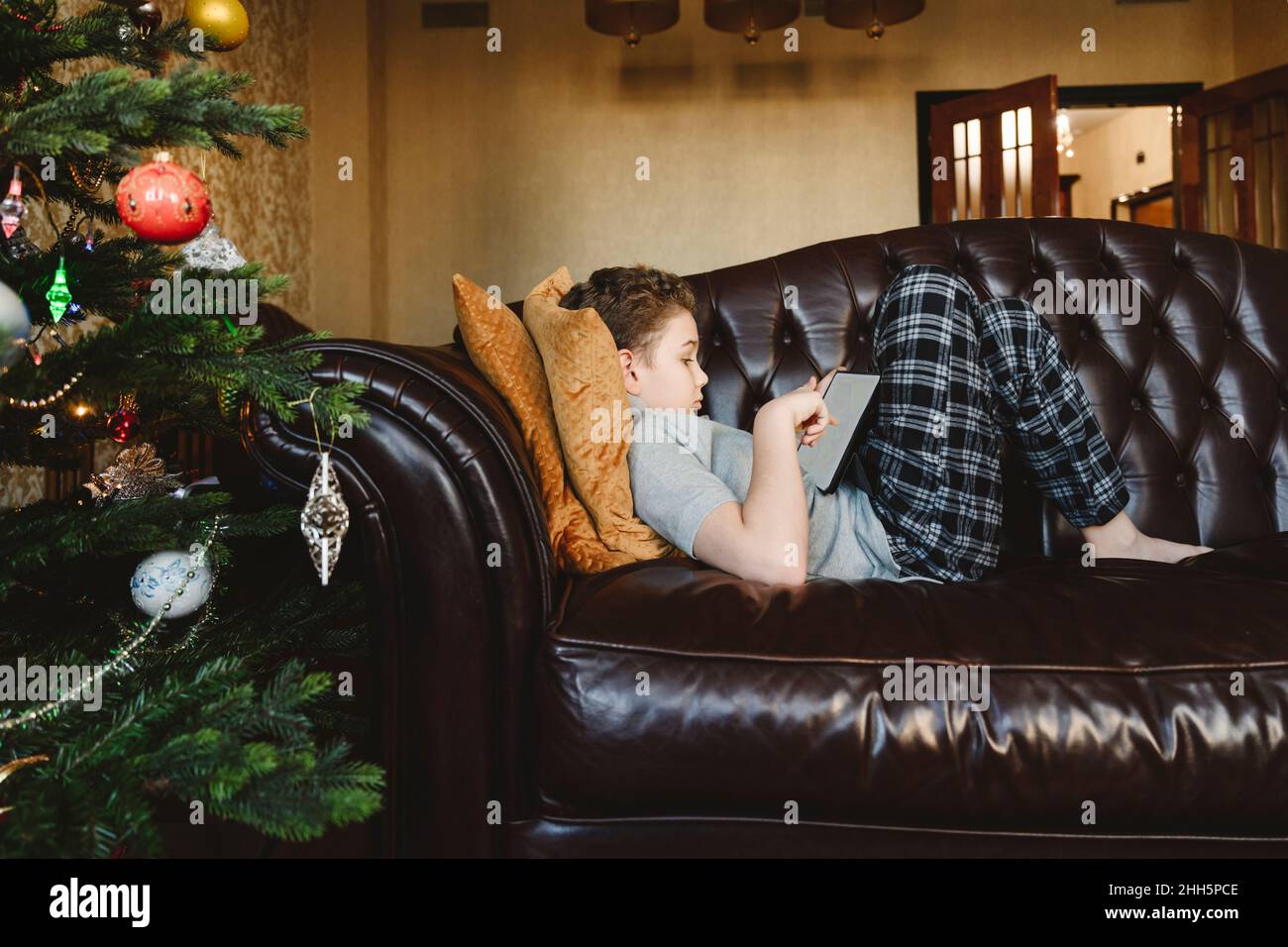 Boy using tablet PC lying on sofa at home Stock Photo