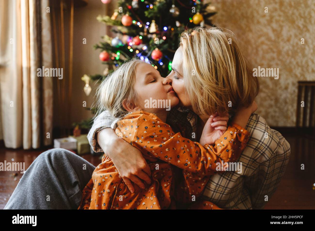 Mother kissing daughter in front of christmas tree at home Stock Photo