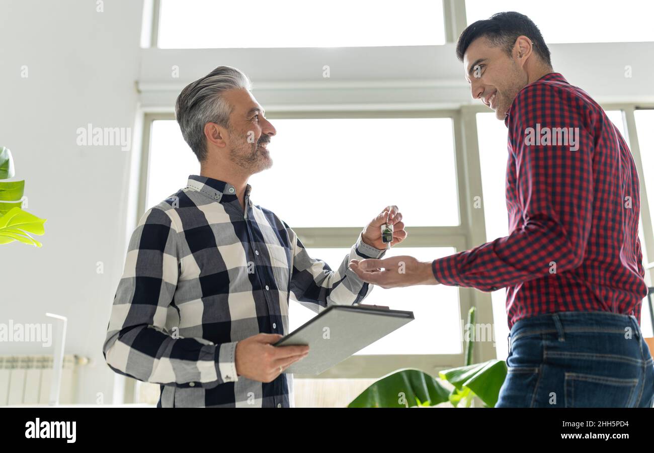Smiling real estate agent giving key to buyer at home Stock Photo