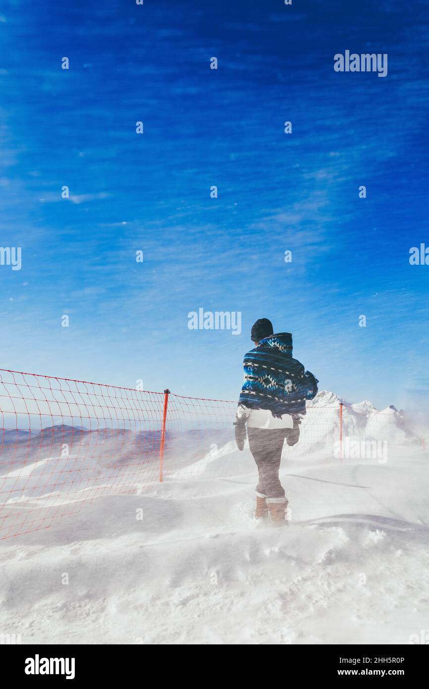 Man with poncho walking toward fence in blizzard Stock Photo