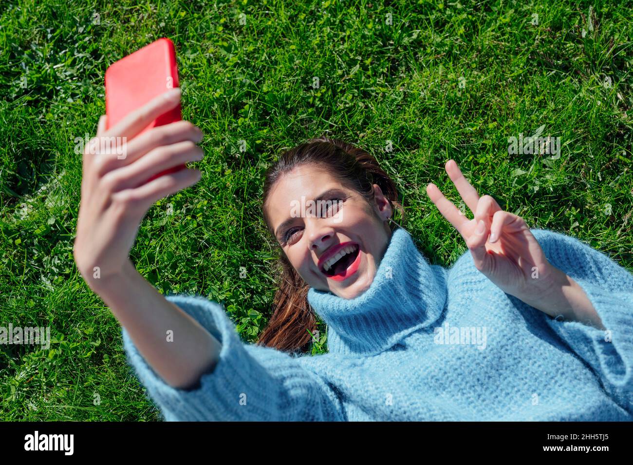Cheerful woman taking selfie lying down on grass Stock Photo