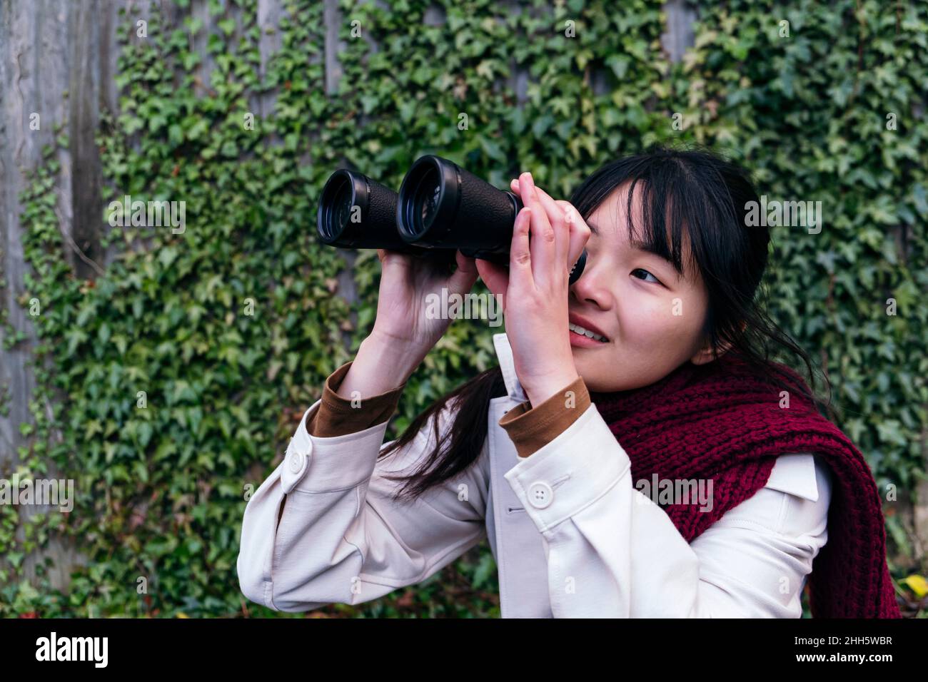 Smiling young woman looking through binoculars Stock Photo