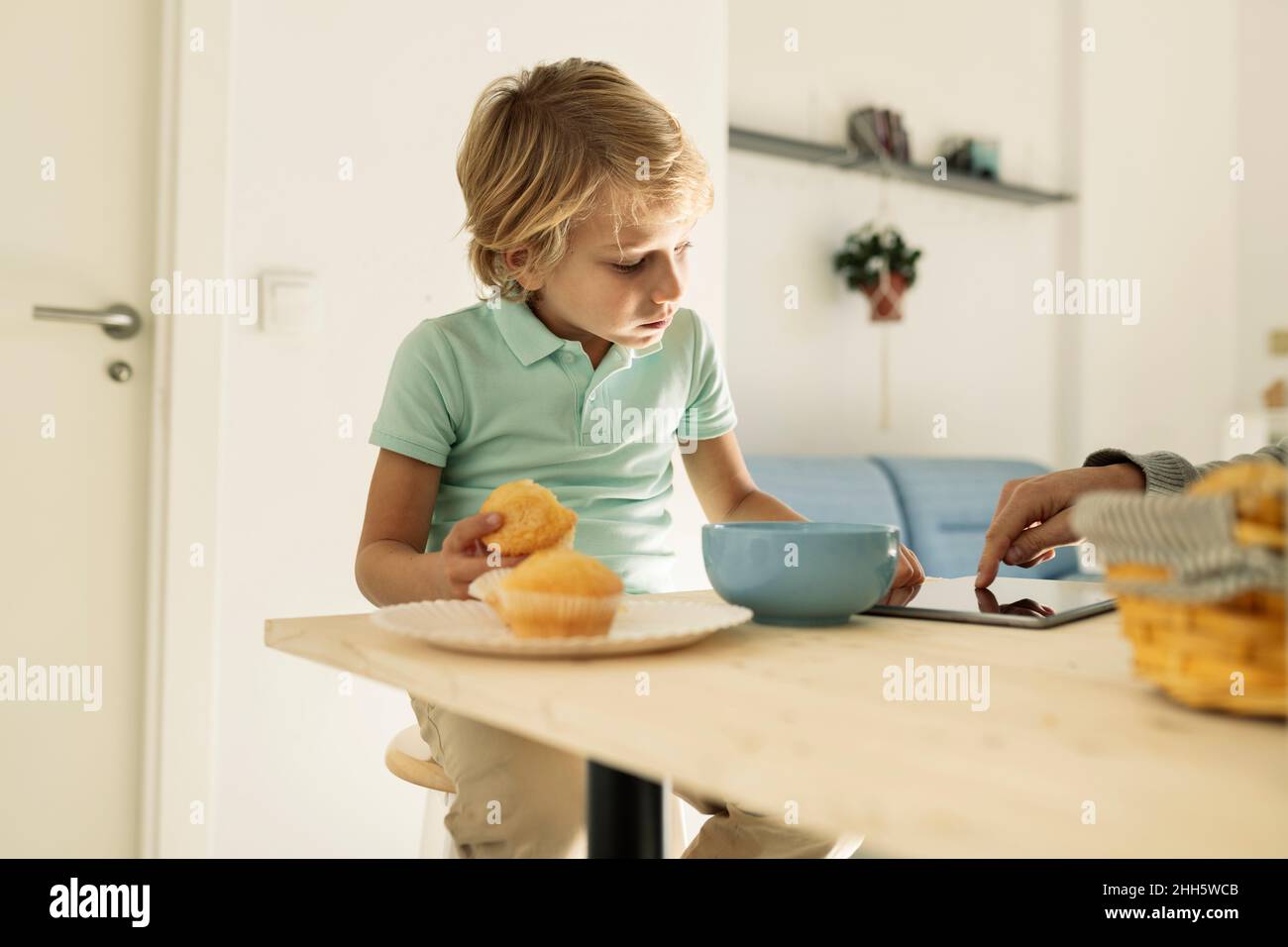 Boy using tablet PC and having cupcake at home Stock Photo