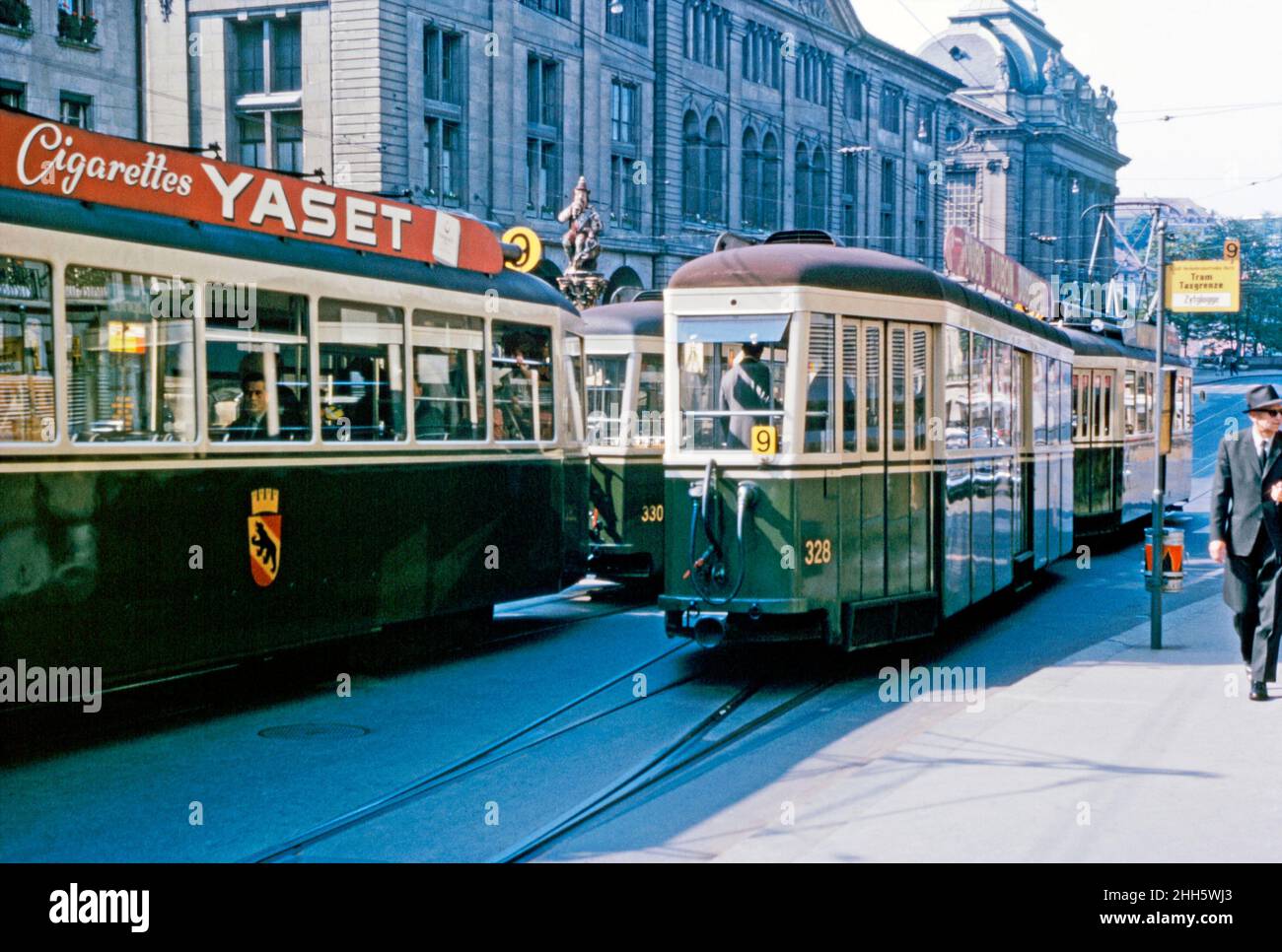 Trams on the number 9 route on the Kornhausplatz (Granary Place) in Bern, Switzerland c. 1960. One tram advertises Yaset cigarettes. Behind the trams the top of The Kindlifresserbrunnen (‘Fountain of the Eater of Little Children’) is visible. This area is now pedestrianised and vehicle free but the trams still run up and down the street. The Bern tramway network began operating in 1890 – today it has five lines. Bern (Berne) is the de facto capital of Switzerland. This image is from an amateur 35mm colour transparency – a vintage 1950s/1960s photograph. Stock Photo