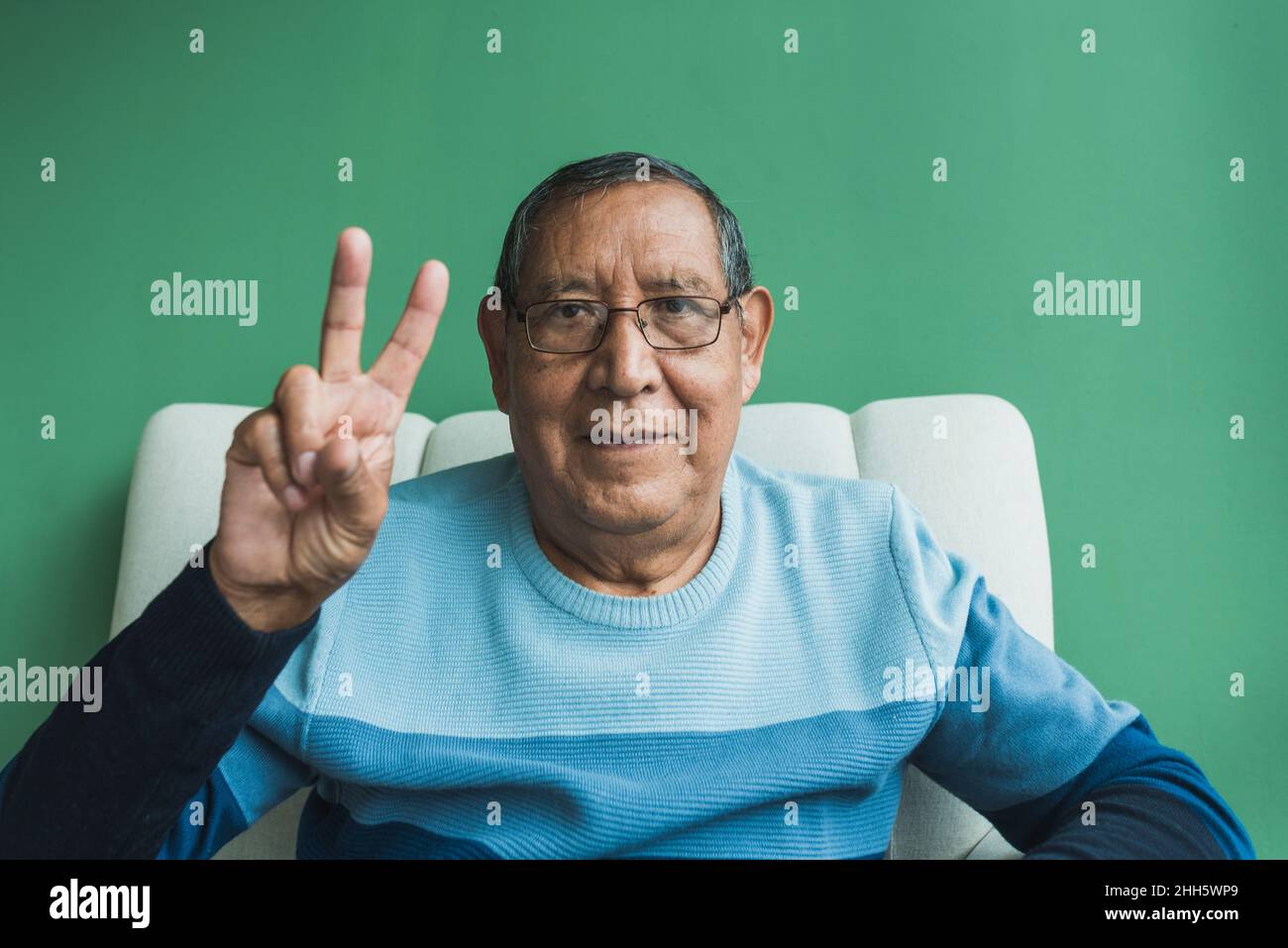 Senior man gesturing peace sign in front of green wall Stock Photo