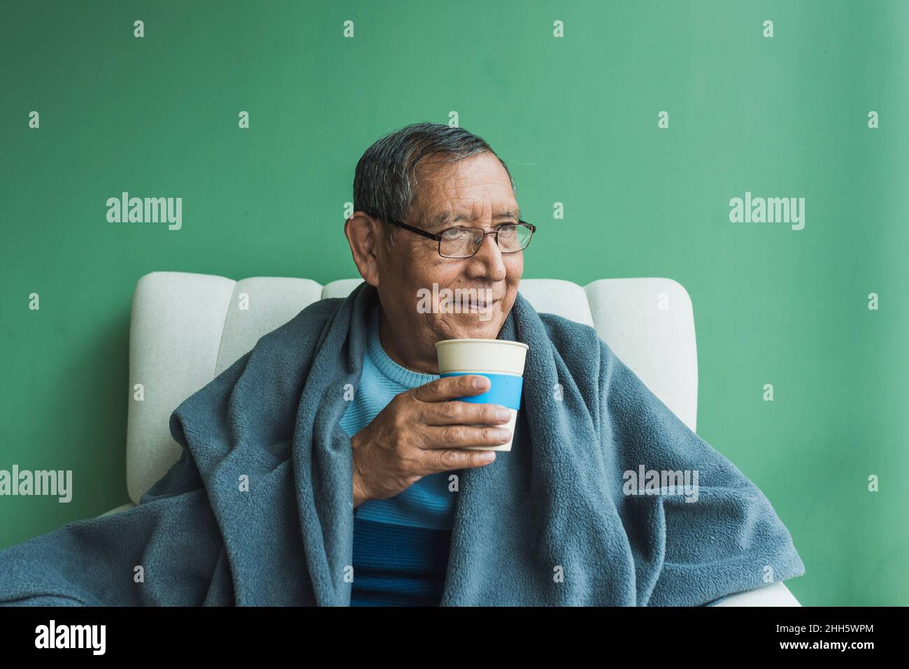 Smiling senior man with disposable coffee cup in front of green wall Stock Photo