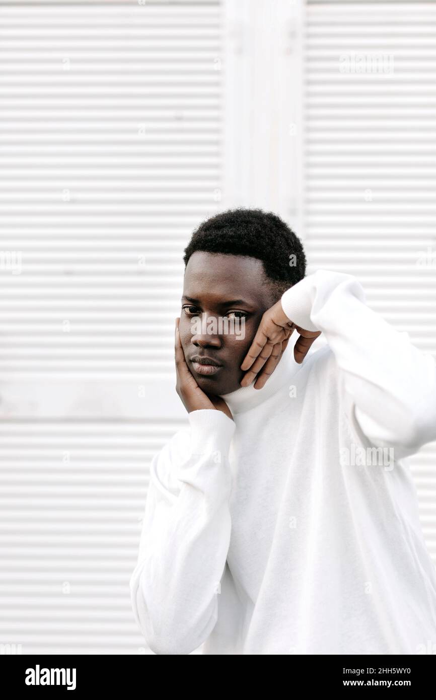 Young man in white sweater touching face in front of white wall Stock Photo
